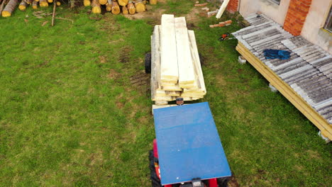 red tractor backing up trailer with sawed wooden boards outside the sawmill, aerial view