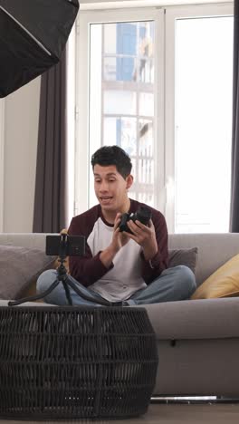 young latin man talking on mobile camera, explaining a photo camera. content creator concept