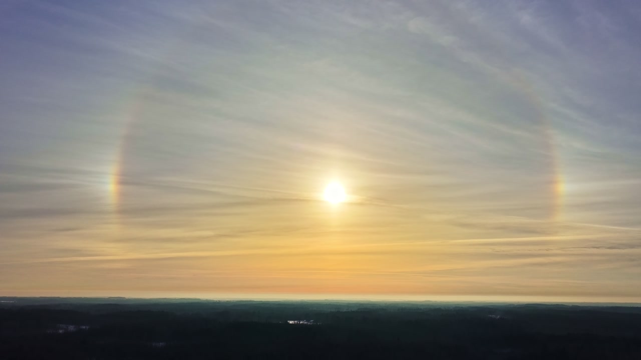 Striking atmospheric optics featuring parhelion sun dogs and circular halos above distant landscape at sunrise with creative lens flares in high altitude view
