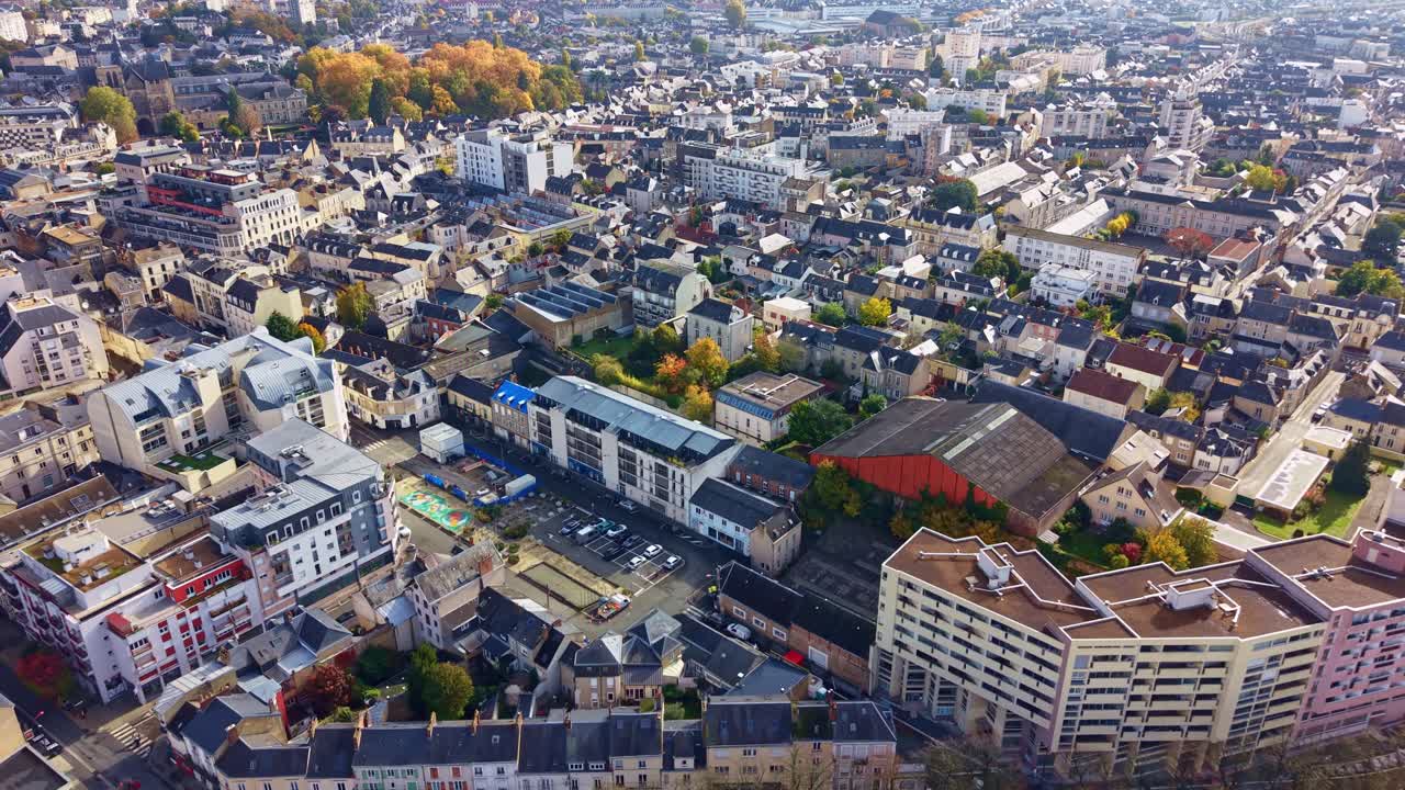 Drone flight over Le Mans, showing residential buildings, curved streets, and autumn-colored trees under a clear sky