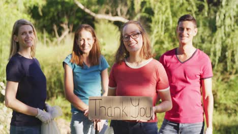 mid adults smiling and looking at camera with woman holding thank you sign during river clean-up day