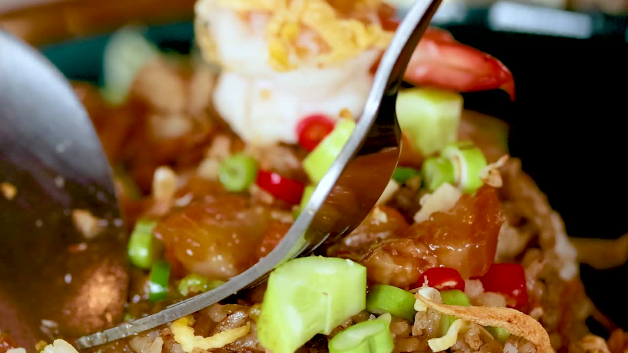 Detailed view of shrimp fried rice with vibrant ingredients being mixed with a fork and spoon.