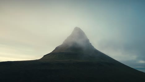 Wunderschöne-Drohnenluftaufnahme-Eines-Einzelnen-Grünen-Berggipfels-Mit-Nebliger-Wolkendecke