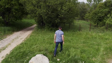 Follow-through-drone-shot-of-a-tourist-walking-in-the-woodlands-of-Tsarichina-hole,-passing-by-a-rock-landmark-in-a-village-in-Bulgaria