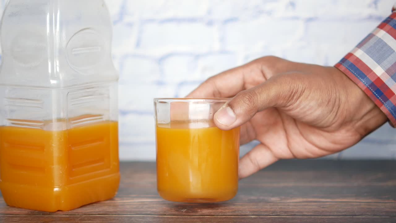 Mano che tiene un bicchiere di succo d'arancia con una bottiglia sullo sfondo