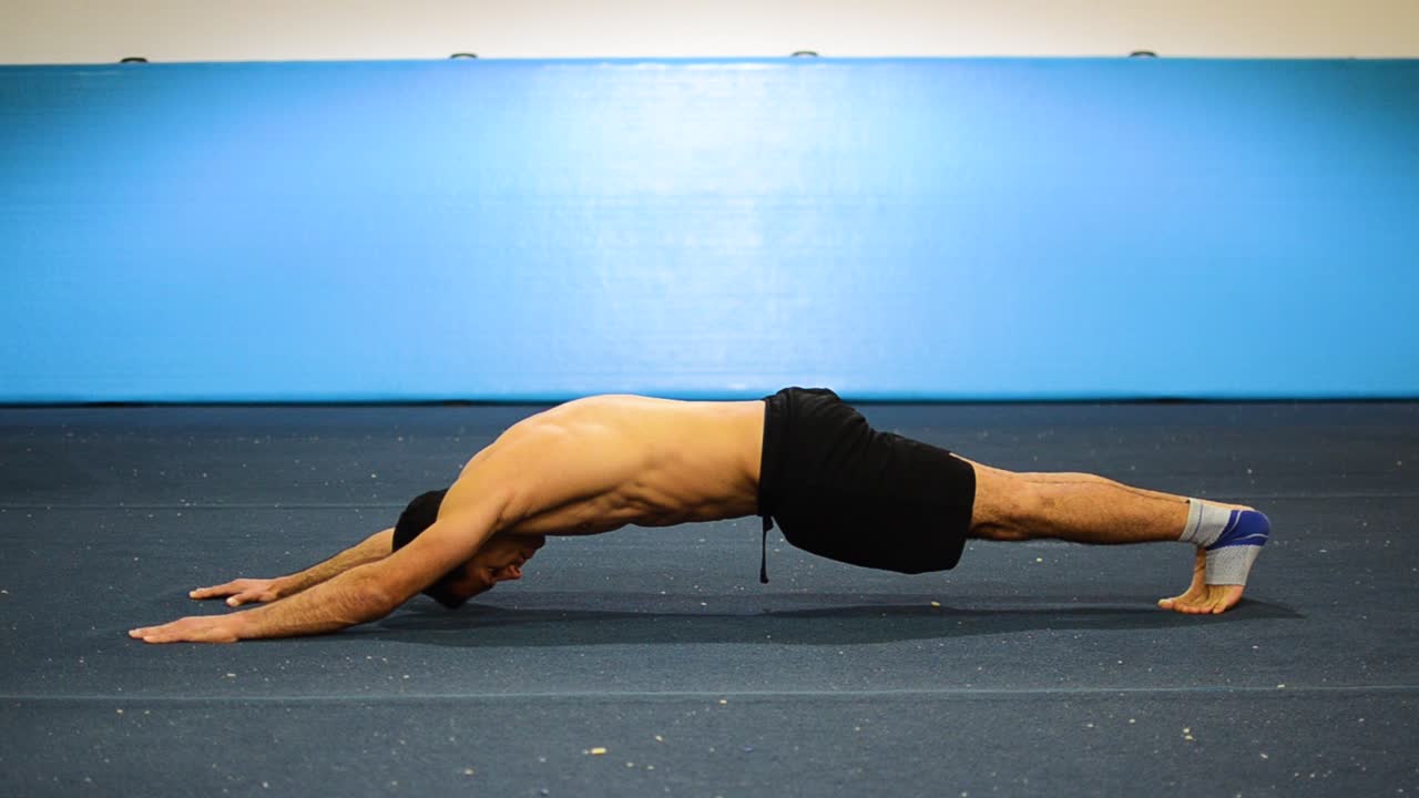 un tipo haciendo una sujeción estática en un gimnasio de gimnasia ejercitando sus abdominales y músculos centrales todavía disparados