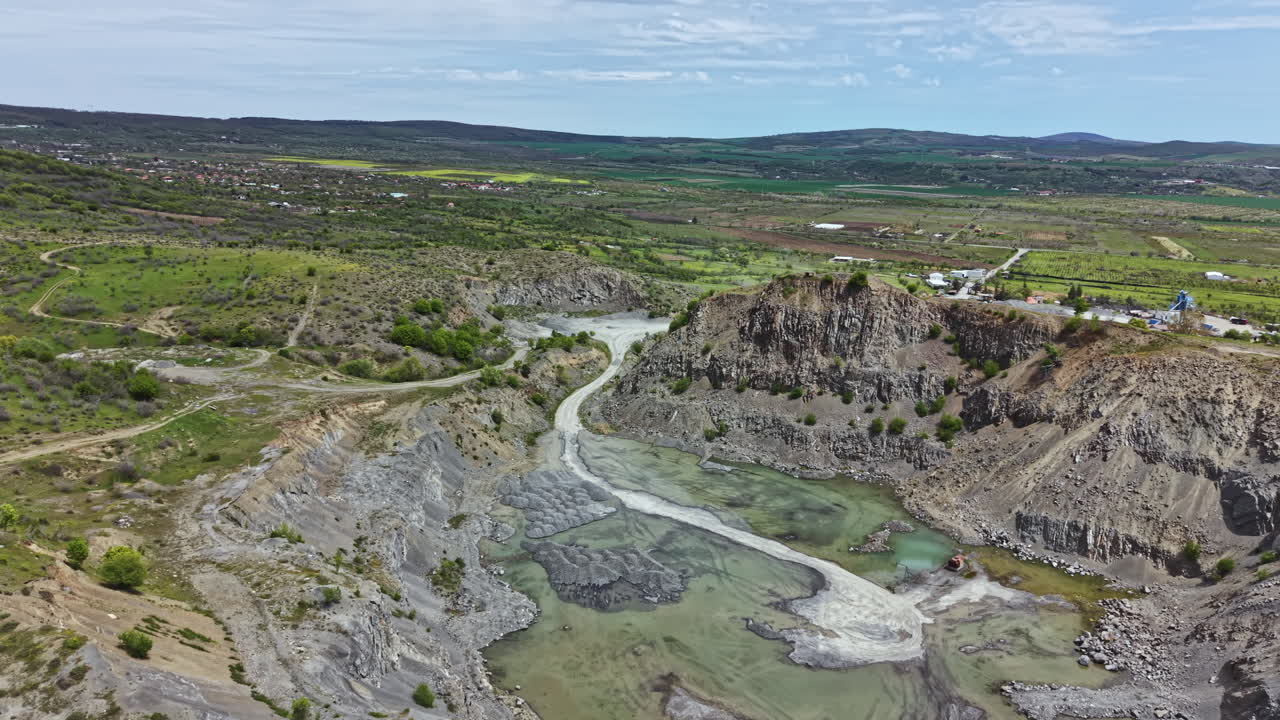 Vista panoramica di una cava circondata da un paesaggio verde e campi, che mette in evidenza le risorse naturali e il processo di estrazione a cielo aperto.