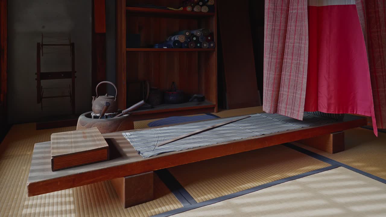 Interiér historické japonské dílny s dřevěným věšákem na kimono (Ikou) a rolemi textilu. Jemné sluneční světlo proniká skrz shoji zástěny, osvětluje tatami podlahu a vytváří.