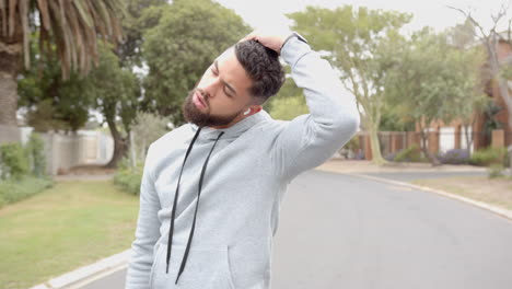 exercising outdoors, man stretching neck on suburban street in casual hoodie