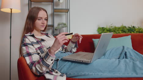 Woman-sitting-at-home-using-credit-bank-card-and-laptop-pc-while-transferring-money-online-shopping