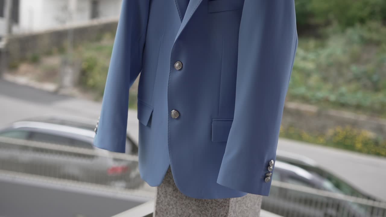 Light blue suit jacket with silver buttons displayed on stone stand outside
