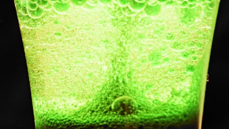 macro shot of sparkling green bubbles moving up in a glass with bright background and some bigger bubbles dripping down