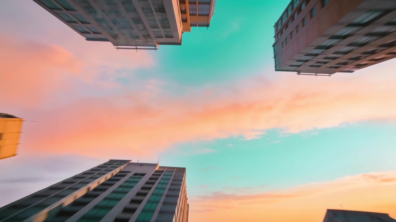 Câmera em nível do chão inclinando-se, revelando uma faixa de nuvens em tons pastel e cores do nascer do sol acima das janelas de arranha-céus.