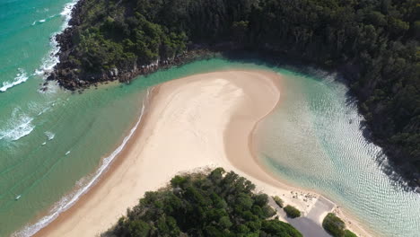 Wide-rotating-drone-shot-of-the-Korogoro-Creek-with-wind-blowing-sand-across-a-sand-bar-at-Hat-Head-New-South-Wales,-Australia