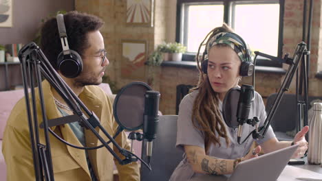 young man and woman wearing headphones sitting at a table with microphones while they recording a podcast 1