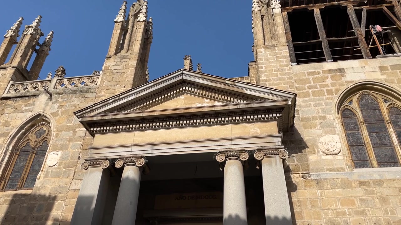 Riprese sul lato della cattedrale di Toledo dove ci concentriamo sulle parti superiori, iniziamo a vedere una cupola, guglie e poi la Puerta del Sol, vediamo grandi finestre e finiamo alla Puerta de los Leones