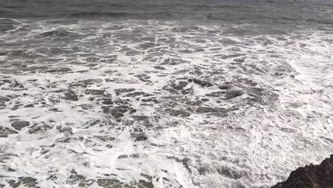 A-panning-shot-of-a-beautiful-sea-where-waves-are-crashing-on-the-boulders-by-the-sea