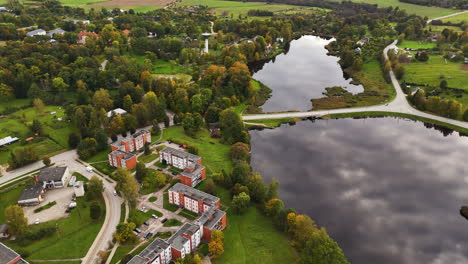 aerial establishing orbit of malpils castle and gardens surrounded by lush trees and walking paths, latvia, clouds reflect in water