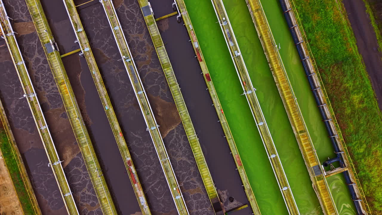 Water treatment process takes place in a facility showing multiple treatment ponds with varied water colors and structures set in an outdoor location