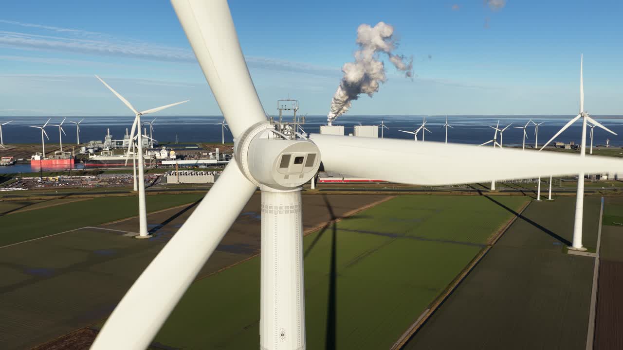 Close-up aerial video showing a spinning wind turbine directly in front of a major data center in Eemshaven, Netherlands. Highlights clean, sustainable power and green IT infrastructure