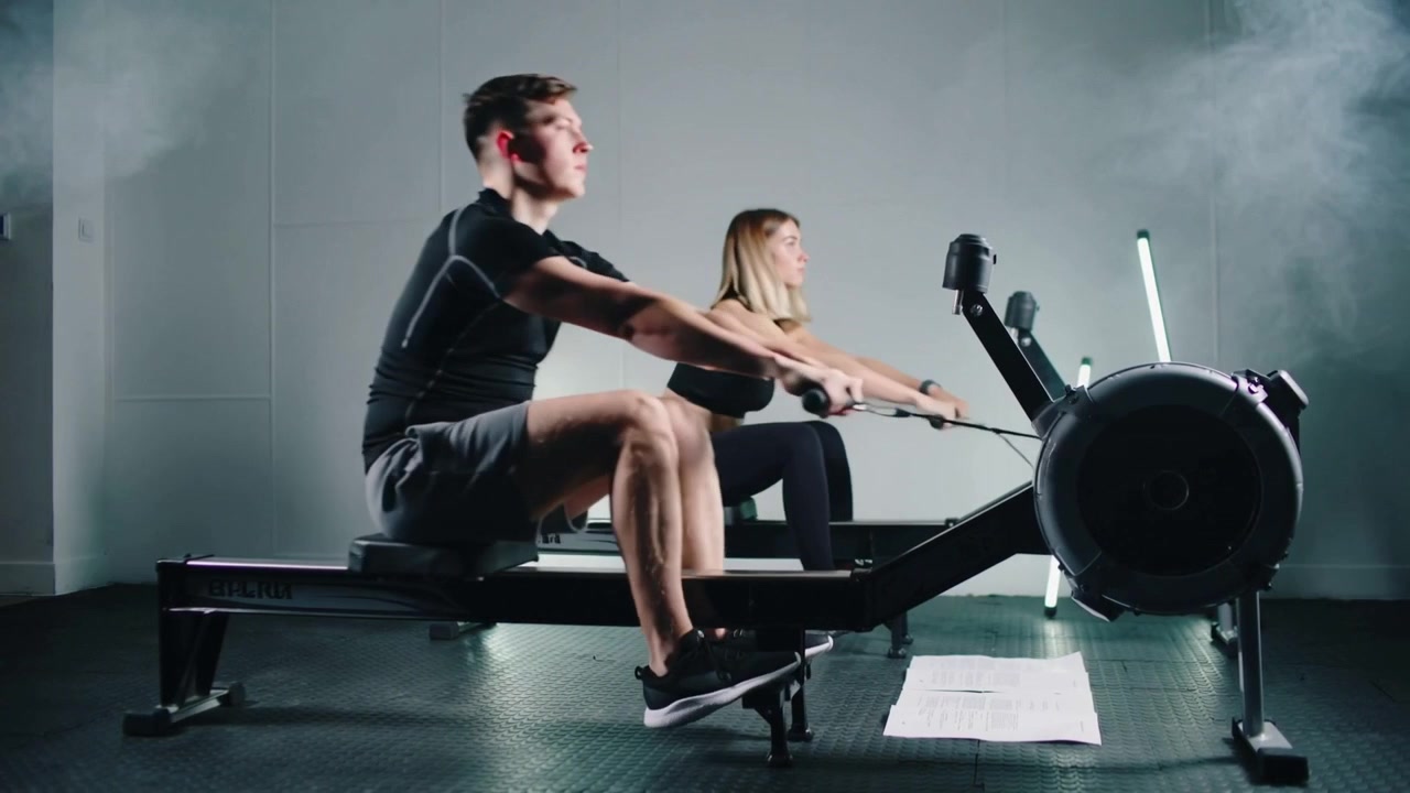 Rowing pair pulling handles on rowing machines in studio following workout plan wearing black gear