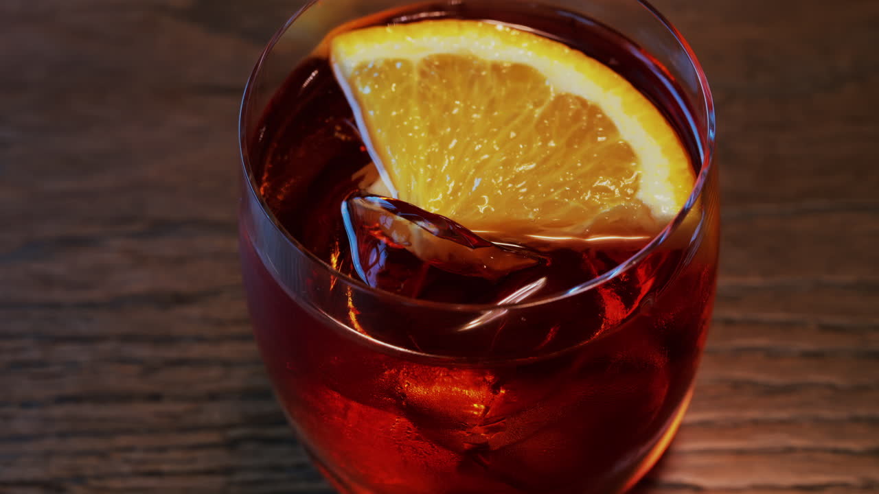 Close up of a Negroni cocktail with orange slice and ice cubes on a wooden table