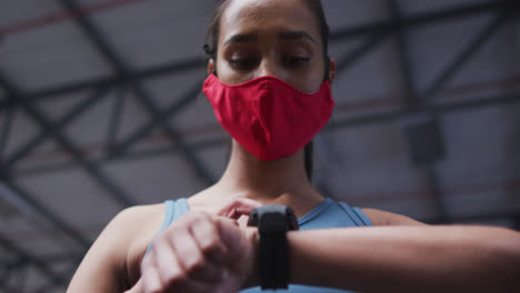 Mujer-De-Raza-Mixta-Con-Mascarilla-Usando-Smartwatch-En-El-Gimnasio