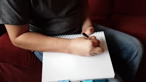 male with a partially amputated index finger on his right hand sat down holding a pen and pad  writing a to do list.