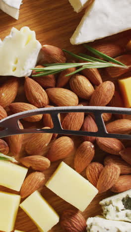 video de quesos duros y blandos variados, nueces y romero con cuchillo en tablero de madera