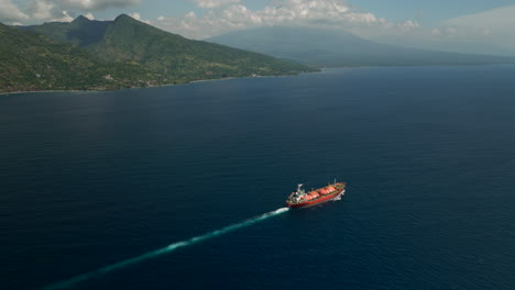 red tanker ship cruise in blue ocean near bali island coastline, high aerial view