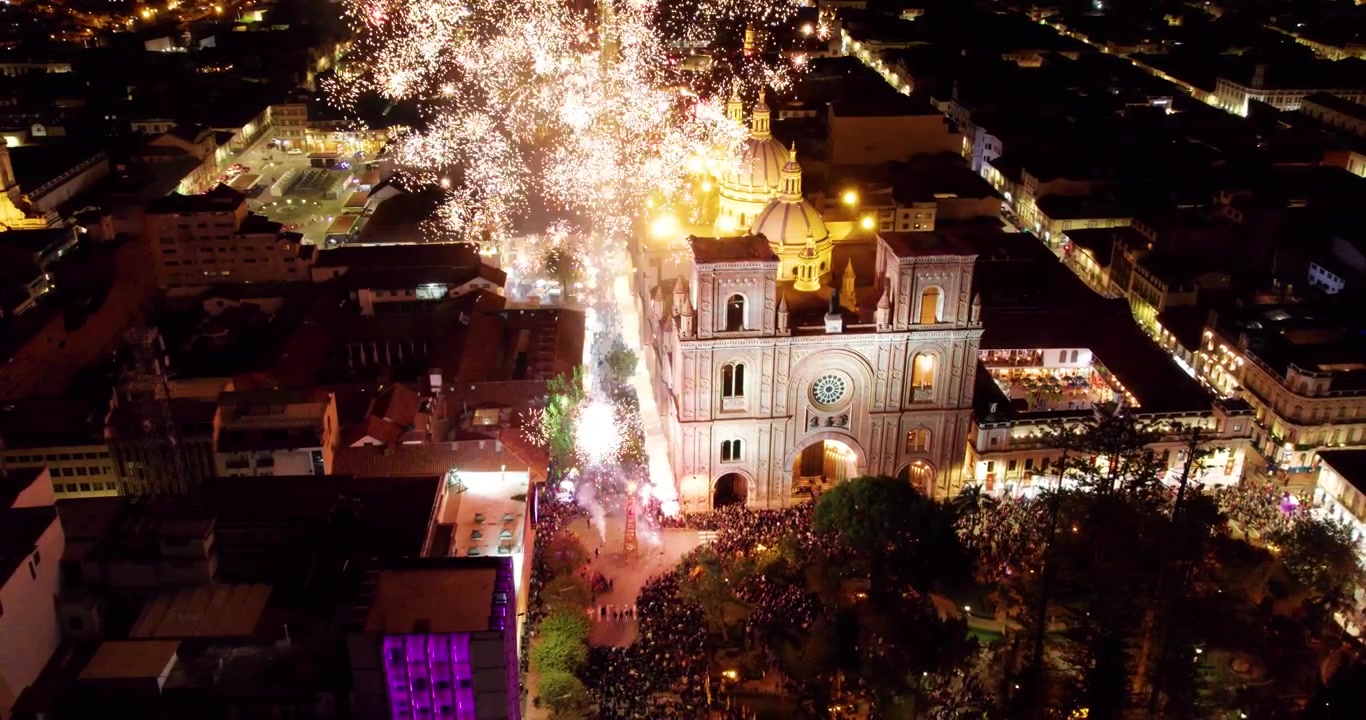 Filmisk drönarflygning tillbaka från katedralen för den obefläckade avlelsen i Cuenca, Ecuador, som avslöjar vackra fyrverkerier som exploderar på den mörka natthimlen under den massiva kulturfestivalen Corpus Christi