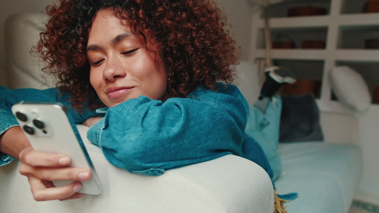 Giovane donna che si rilassa sul divano e scorre lo smartphone