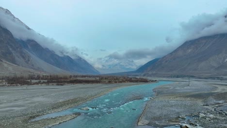 Aerial-View-of-tranquil-scene-of-a-river-winding-through-a-mountain-valley-with-overcast-skies-and-snow-capped-peaks