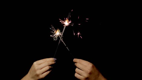 sosteniendo las manos y agitando fuegos bengalíes. vela de chispas de año nuevo ardiendo sobre un fondo negro