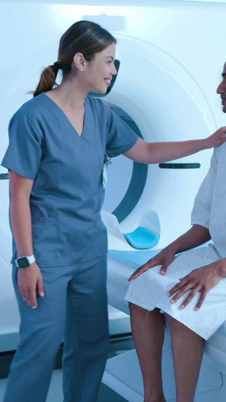 Video verticale: Paziente in camice che entra e si siede sul lettino dello scanner mentre un tecnico in divisa medica lo guida per la scansione.