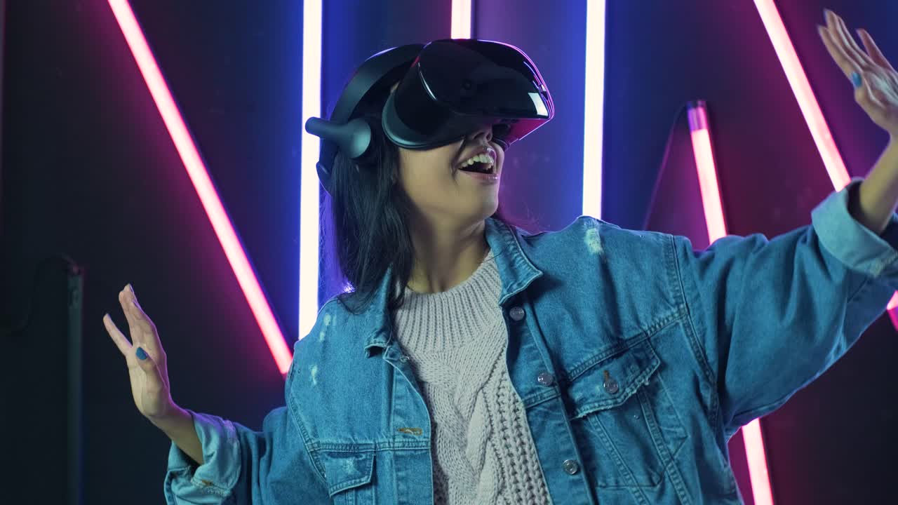 giovane donna scioccata, si guarda intorno e si chiede come incredibile nell'auricolare vr. casco di realtà virtuale su sfondo di illuminazione a colori