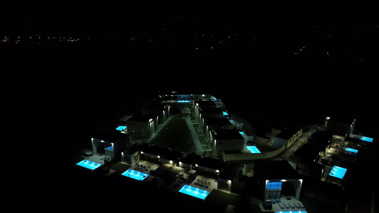 Aerial flyover illuminated pools and vacation homes, night in Rhodes, Greece