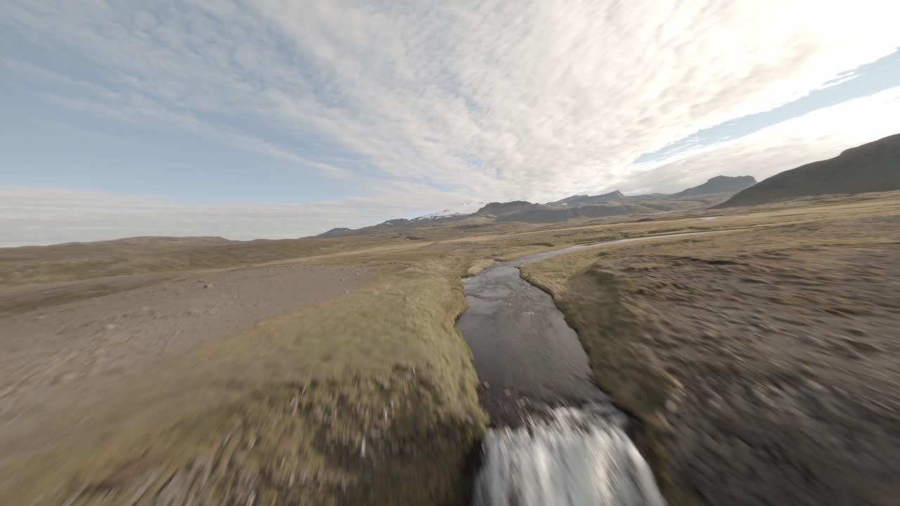 fotografía aérea fpv que marca y se dirige hacia un arroyo y sube a una cascada para revelar un vasto valle y cordillera en islandia