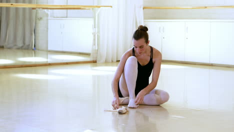 portrait of ballerina is sitting and is putting on her dance shoes