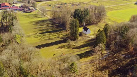 Grünes-Ackerland-Mit-Pferden-Und-Einer-Kirche-In-Südbayern,-Aufgenommen-Von-Oben-Als-Blick-Nach-Oben-Mit-Dolly-Zoom-Effekt-Auf-Die-Kleine-Kapelle