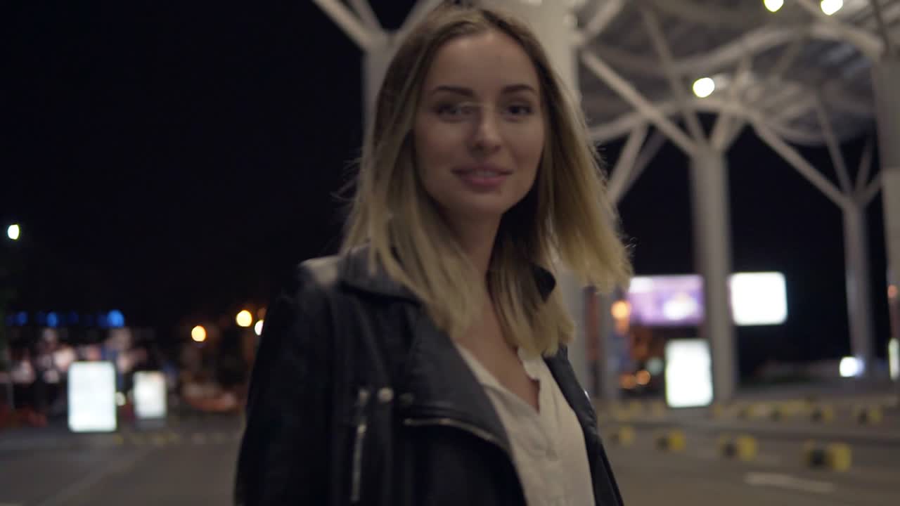 young blonde woman in jeans and black leather jacket jumping on yellow  street bumpers at night, having fun 2