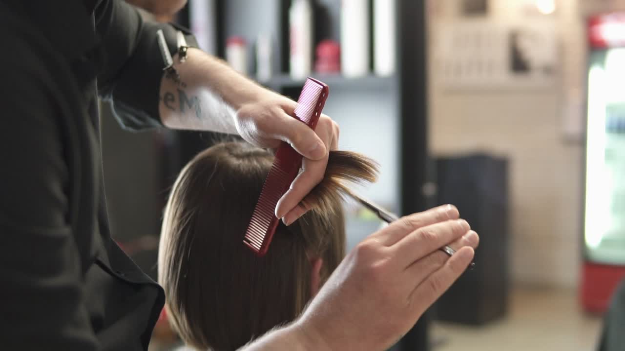 Close Up view of a hairdresser's hands cutting hair with scissors. Young woman getting her hair dressed in hair salon