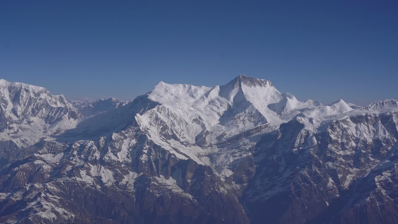 Footage of snow-covered Himalayan range captured from an airplane. Shows dramatic ridges, clouds, and vast natural scenery