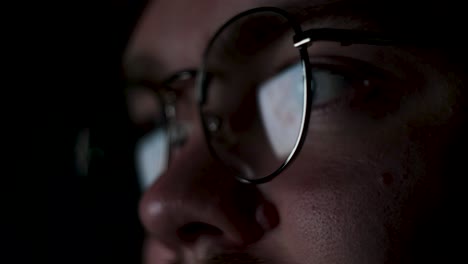 person wearing glasses looking at a screen in the dark