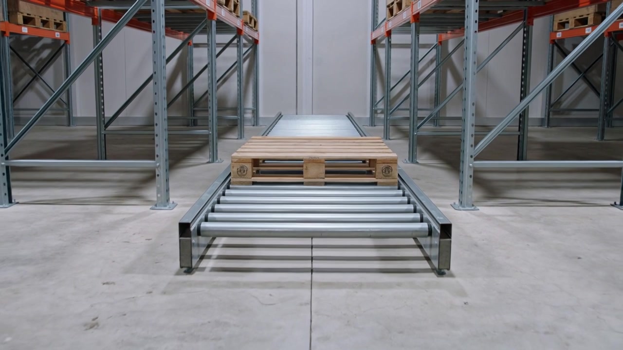 Nastro trasportatore che avvia il movimento di un pallet di legno verso i rulli anteriori in un corridoio con scaffalature.