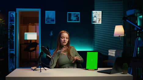 una joven estrella de internet sonriente presenta un modelo de tableta de pantalla verde