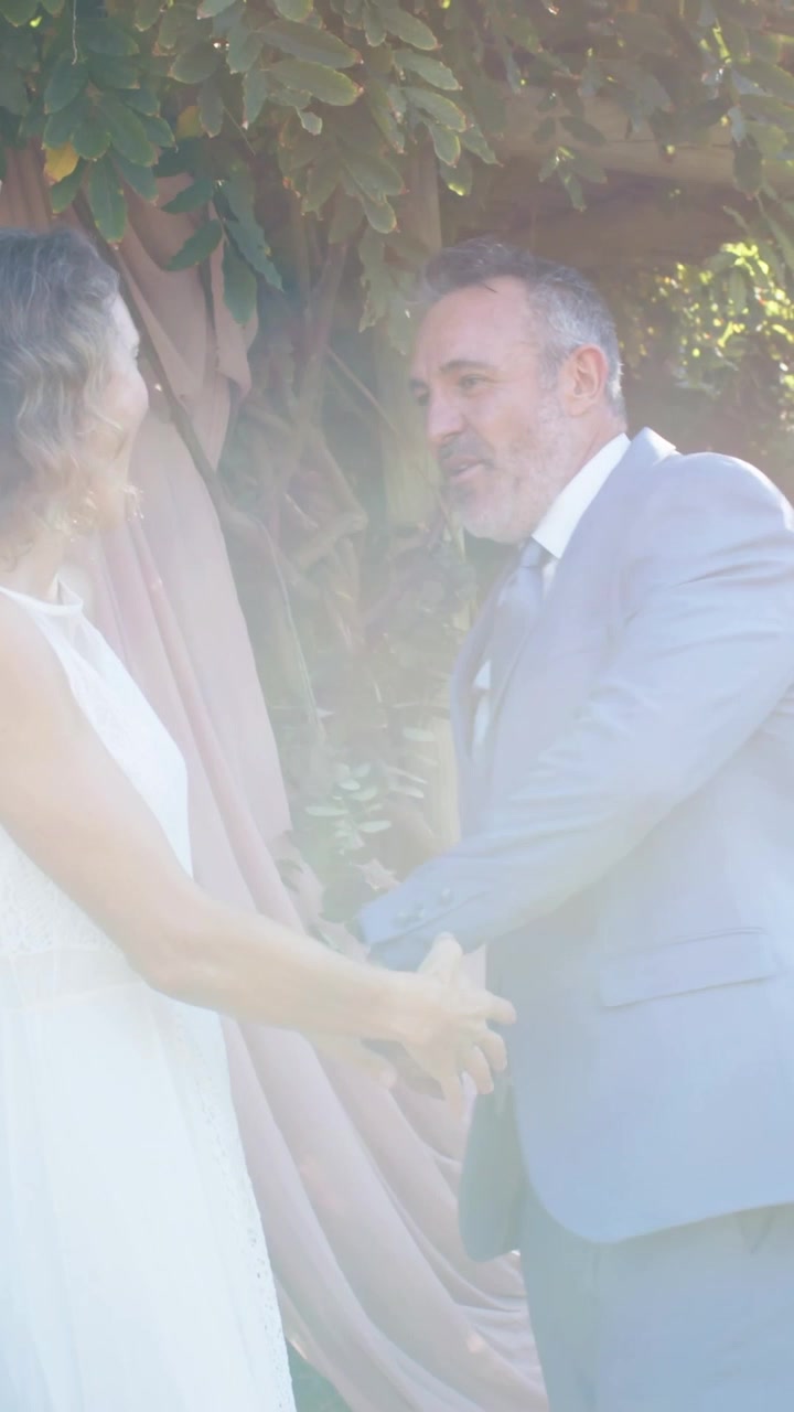 Video vertical: Hombre de traje azul caminando hacia una mujer con vestido blanco, girando en una ceremonia en el jardín.