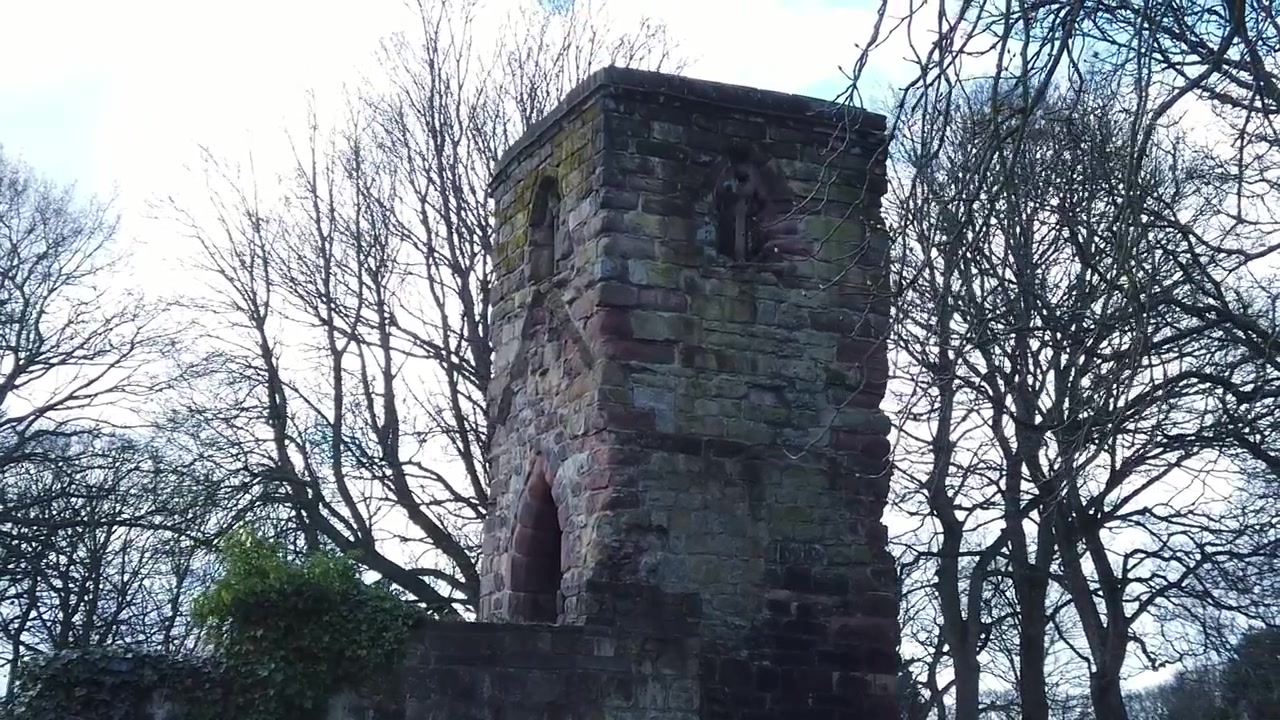 Exterior da torre de pedra da pacífica e histórica Windleshaw Chantry em câmera lenta, ao redor das ruínas, contra o céu azul.