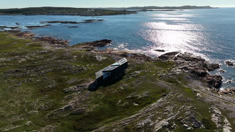 long studio modern architecture overlooking atlantic views with glistening sunlight reflecting on fogo island from an aerial tilt down push in drone shot, newfoundland, canada