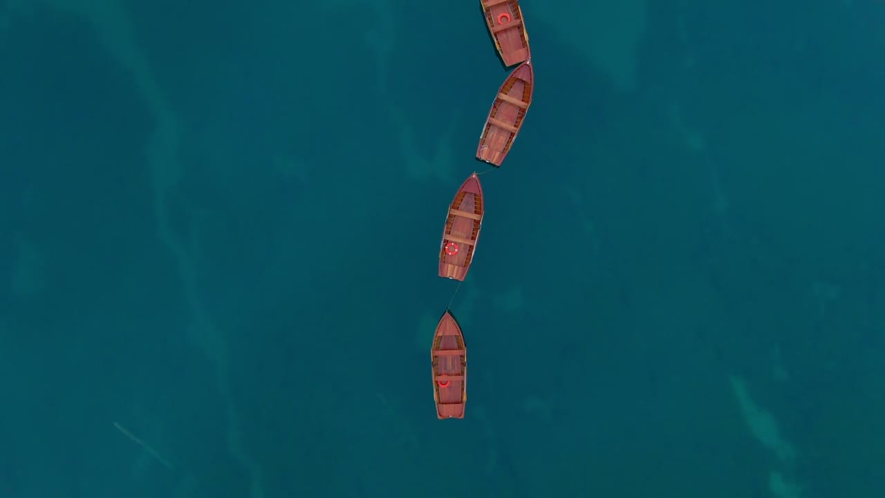 A top down shot lifting up and rotating to reveal mountains from boats on Lago di Braies.